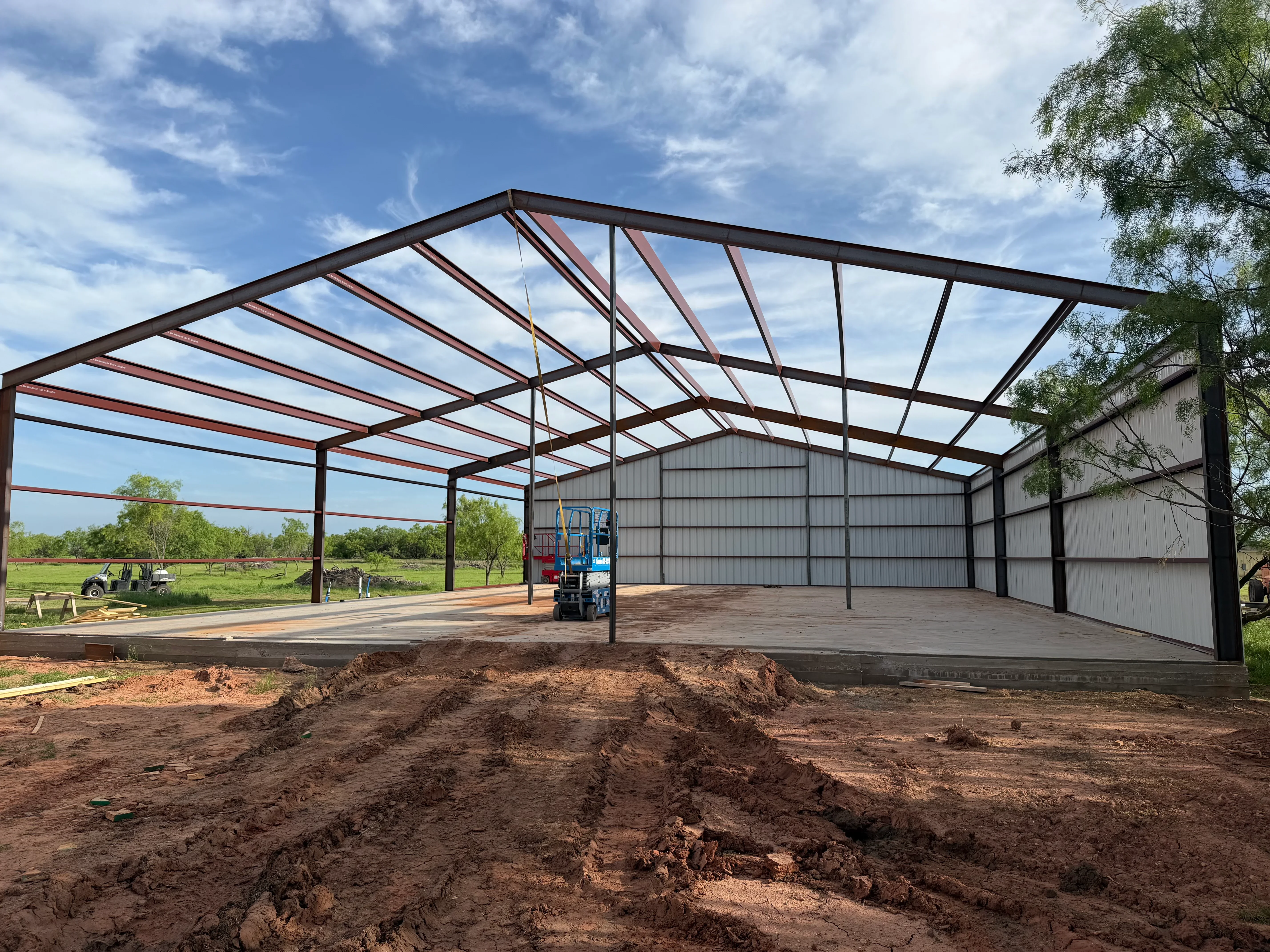 Steel frame agricultural building with black structure, red bracing, concrete slab, and metal paneling