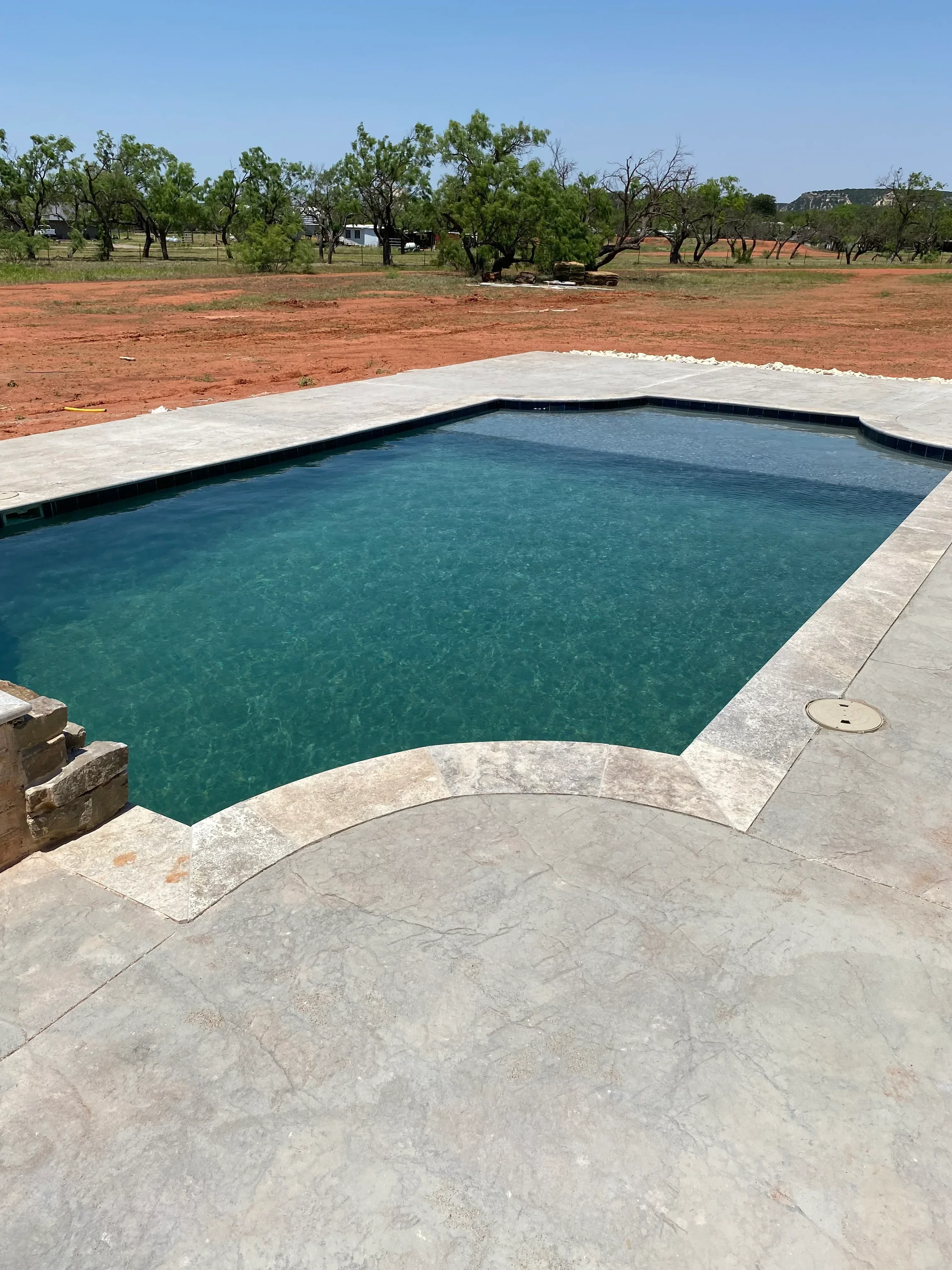 Completed swimming pool with turquoise water, white plaster finish, and concrete decking