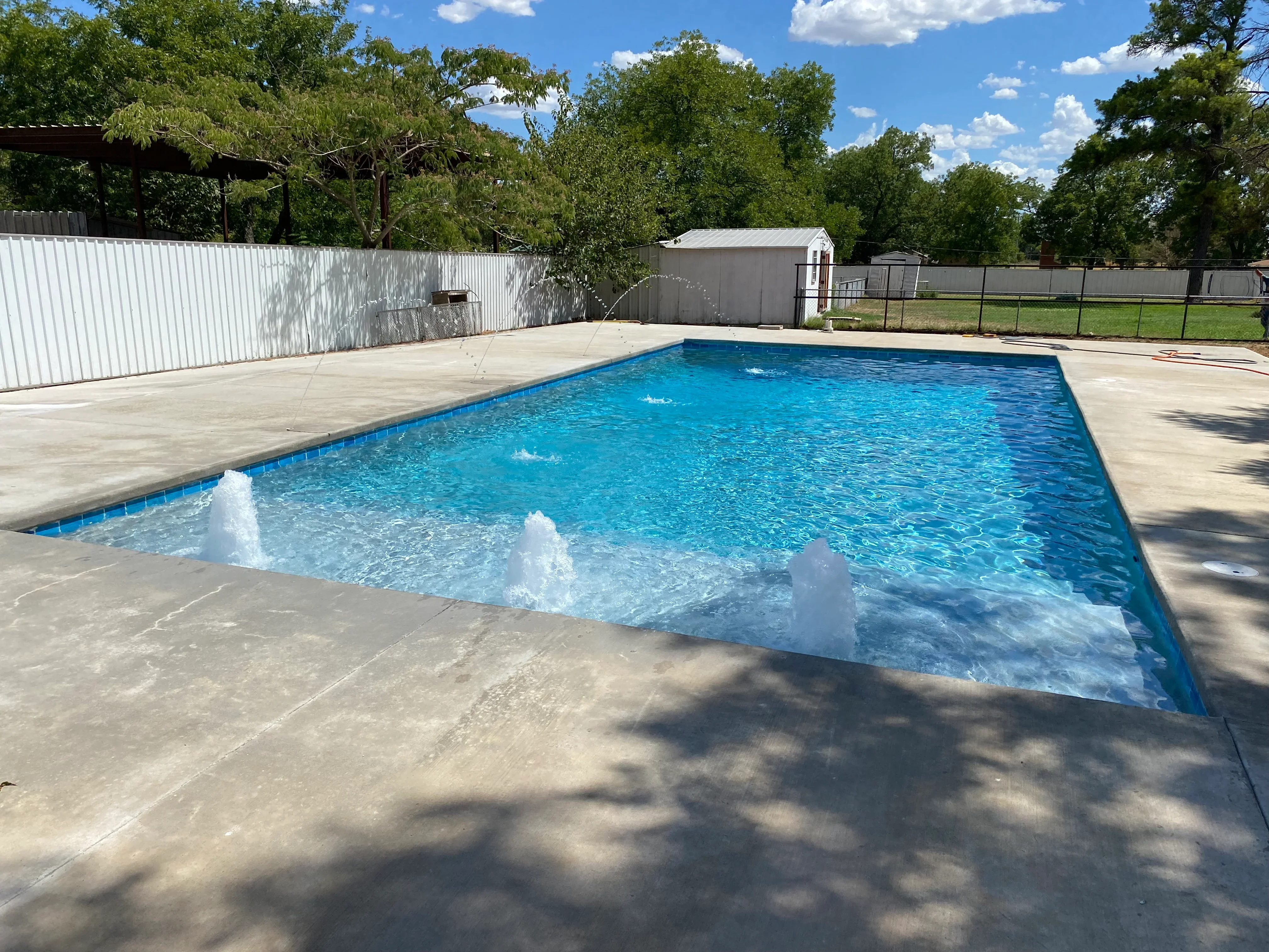 In-ground swimming pool with concrete deck, blue interior finish, and water jets