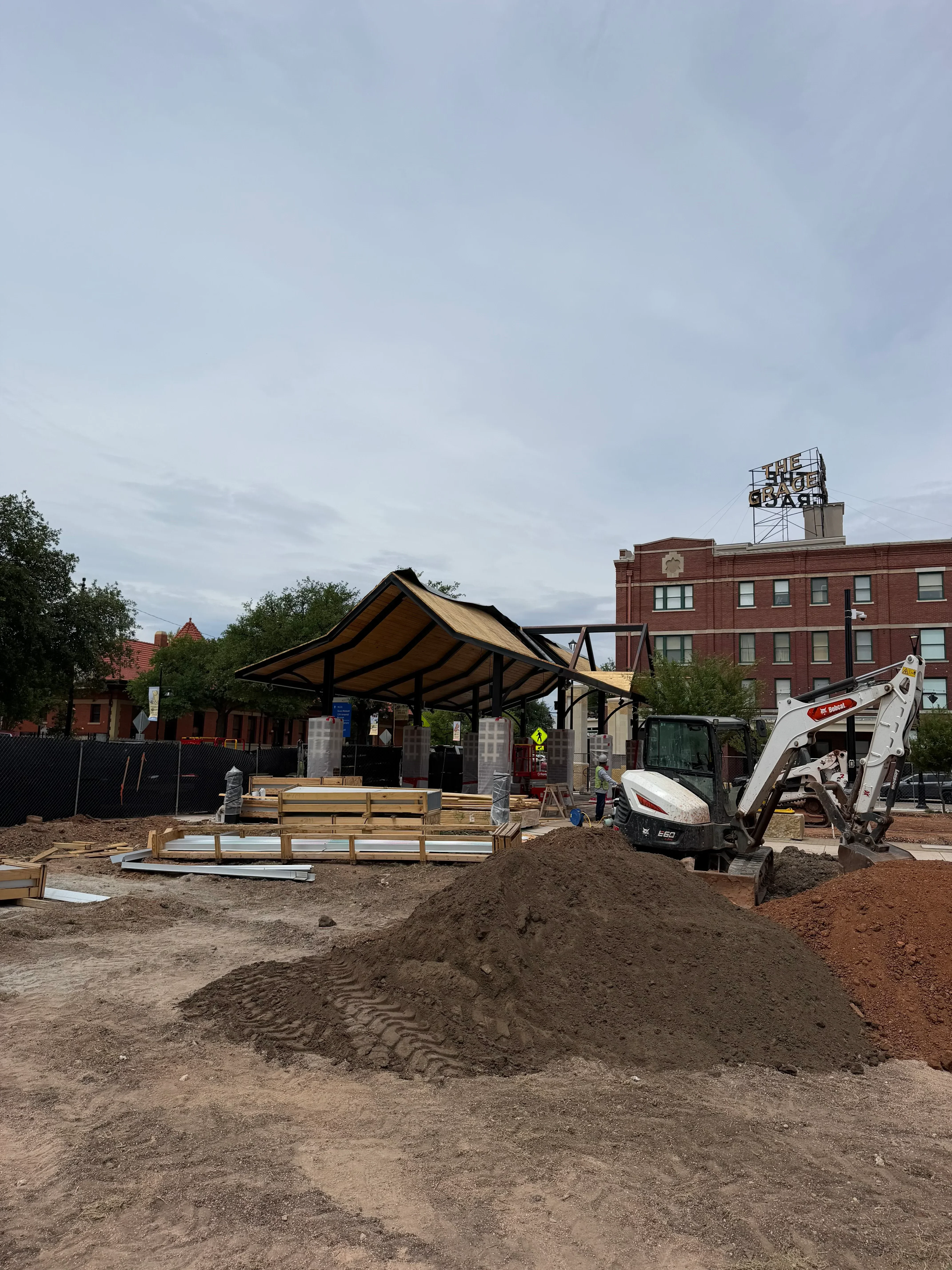Excavator and boom lift operating on urban construction site with brick buildings