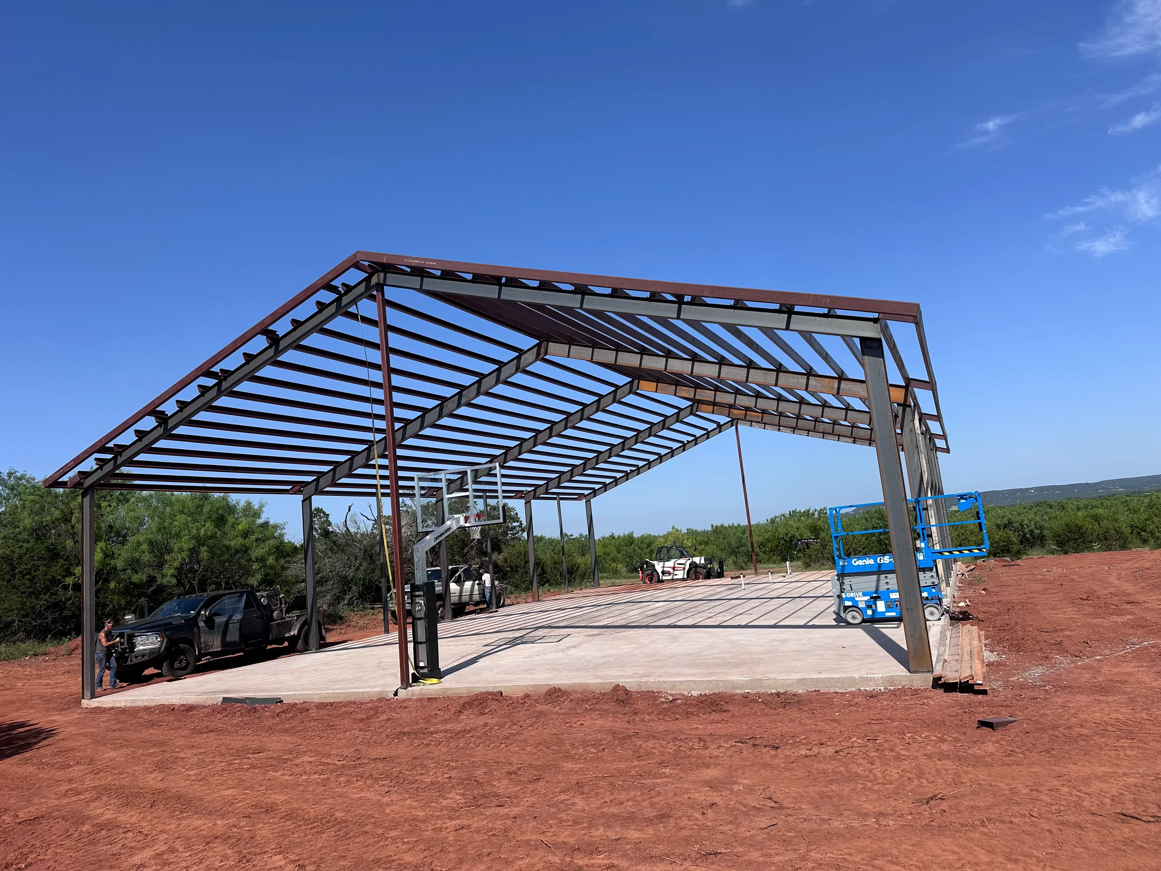 Steel carport frame with horizontal louvers and concrete pad, vehicles parked underneath